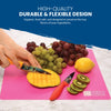 A person slices a mango on a pink cutting mat from the Slice Bright Flexible Cutting Mats - Set of 6 by Chef's Vision, surrounded by grapes, a lemon, and kiwi slices. Text highlights the high-quality, durable, and flexible design of these BPA-free, anti-bacterial cutting mats.