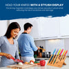 In the kitchen, a woman chops vegetables as a man cooks, with the Chef's Vision BEHOLD Magnetic Kitchen Knife Block featuring colorful knives prominently displayed on the counter, adding a touch of stylish decor.