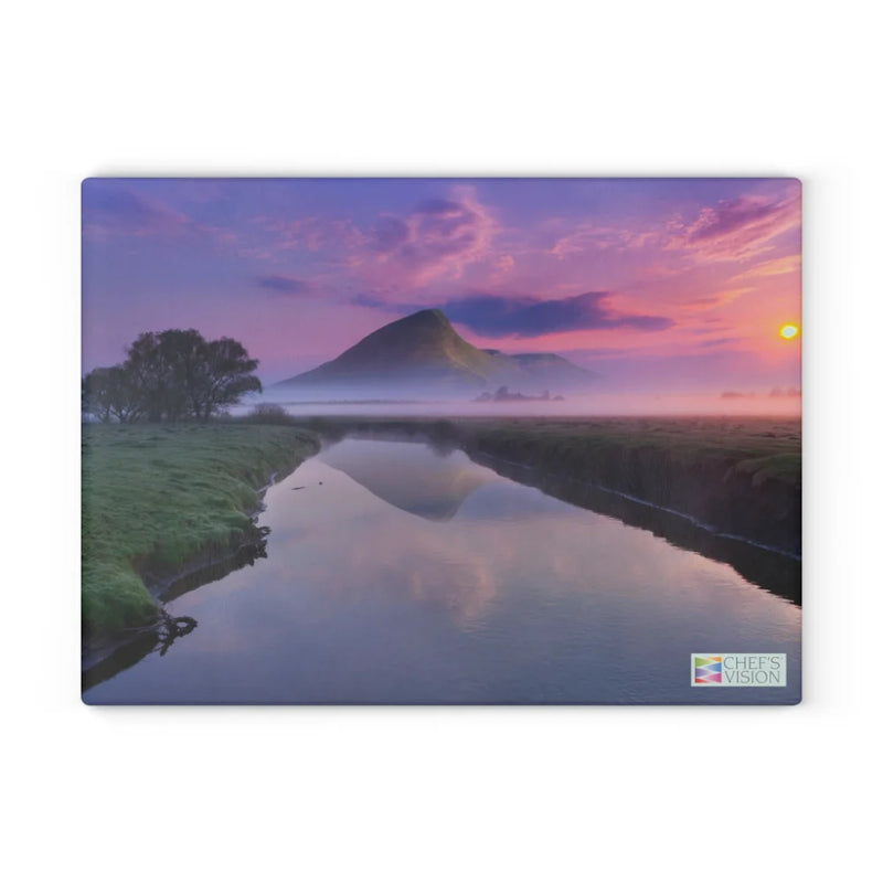 A calm river reflects a misty mountain at sunrise under a purple and orange sky—scenic imagery that makes the Chef’s Vision SliceBright Landscape Glass Cutting Board a perfect way to brighten up your kitchen counter.