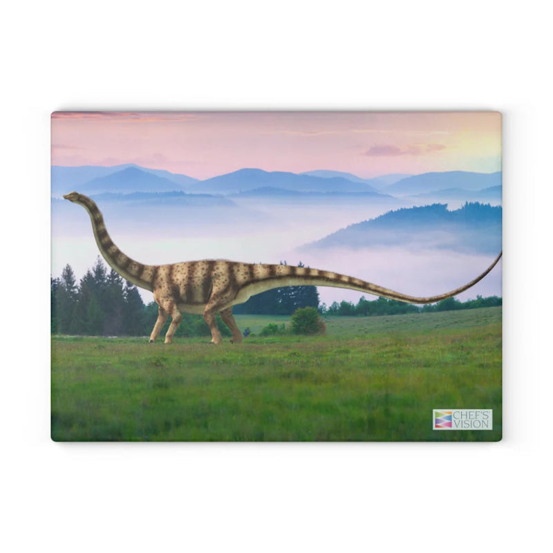 The SliceBright Jurassic Glass Cutting Board by Chef's Vision features a long-necked dinosaur on a grassy field at sunrise, with misty mountains and trees—stunning artwork to brighten any kitchen counter.