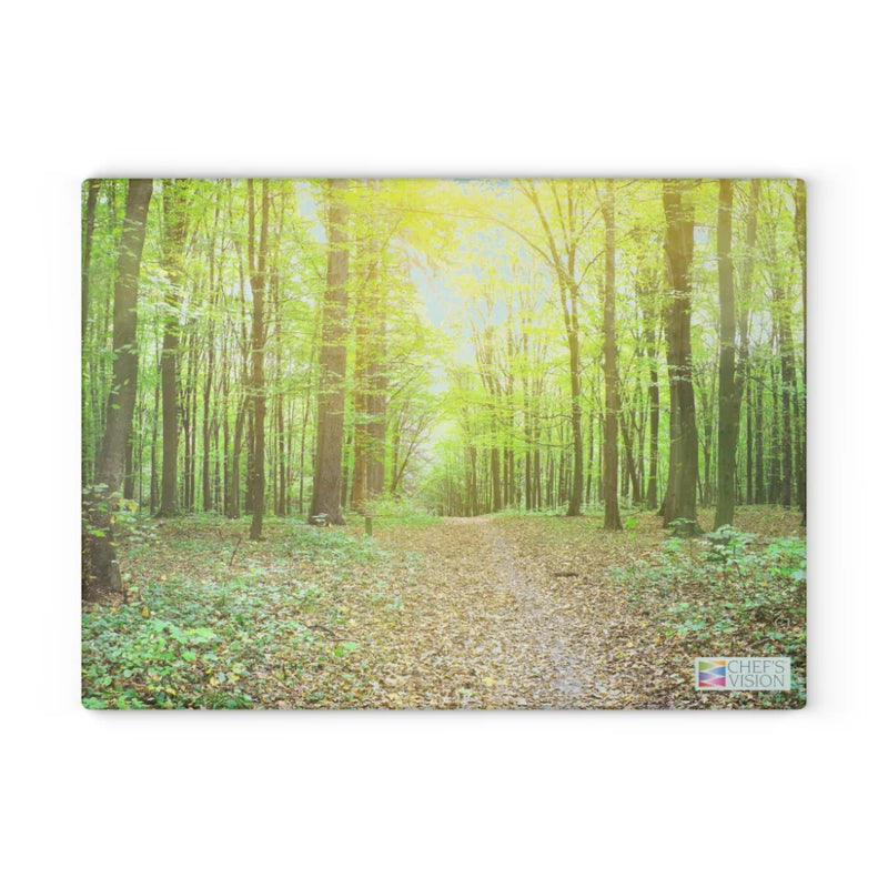 A sunlit forest path lined with tall green trees and scattered leaves is depicted on the SliceBright Landscape Glass Cutting Board by Chef's Vision, featuring a discreet Chef's Vision logo in the bottom right corner.
