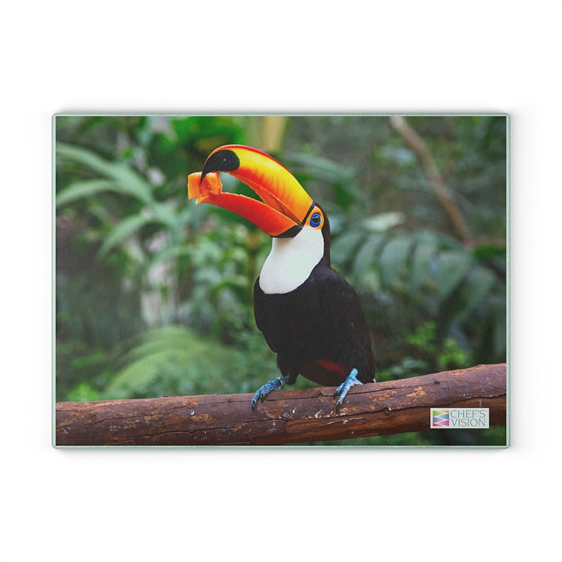 A toucan perched on a branch in the jungle, near a Chef's Vision SliceBright Wildlife Glass Cutting Board.