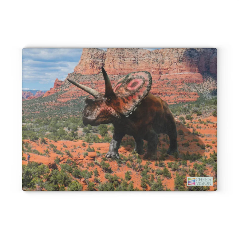Bring prehistoric charm to your kitchen with the Chef's Vision SliceBright Jurassic Glass Cutting Board, featuring a vibrant triceratops with a decorative frill on red rocky terrain and desert cliffs. Perfect for adding style to your countertop.