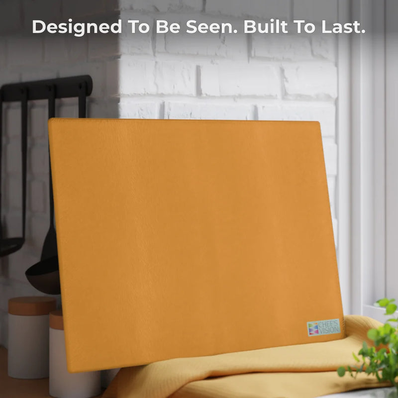 Chef’s Vision SliceBright Color Glass Cutting Board in yellowish-orange sits on a kitchen counter, with the text “Designed To Be Seen. Built To Last.” displayed above it.