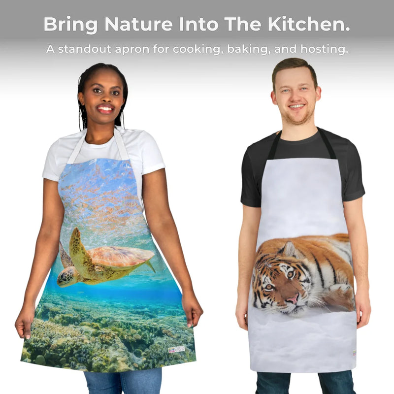 Wearing Chef's Vision Wildlife Aprons, two people display animal-inspired designs: one with an underwater sea turtle, the other featuring a tiger in snow. Crafted from durable polyester canvas, these kitchen aprons bring nature-themed art to cooking.