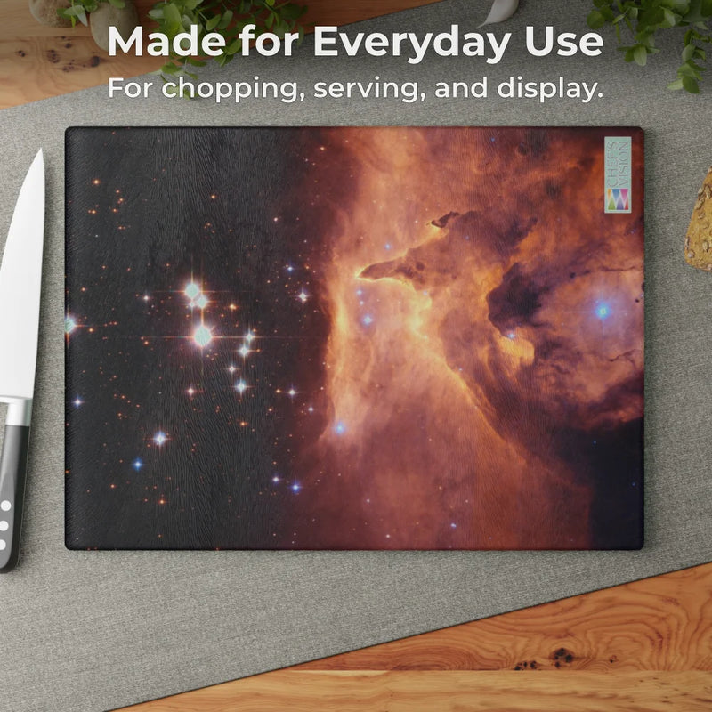 The Chef's Vision SliceBright Cosmos Glass Cutting Board, featuring cosmic imagery, is shown on a kitchen counter beside a knife, with text emphasizing its durable tempered glass design for everyday use.