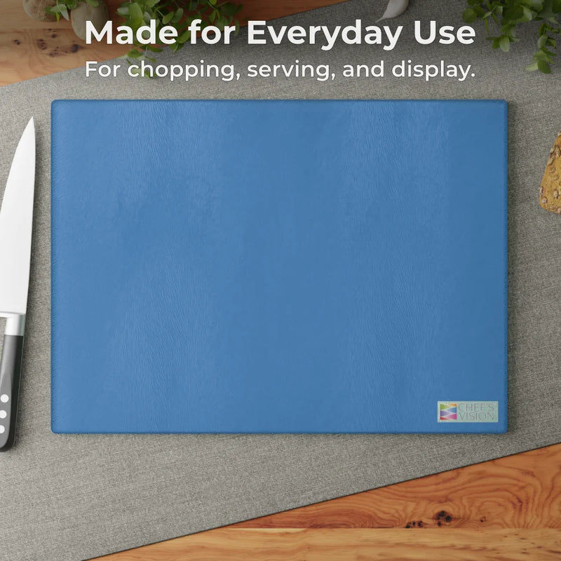 The Chef's Vision SliceBright Color Glass Cutting Board, featuring textured blue tempered glass, sits on a gray placemat beside a kitchen knife—perfect for chopping, serving, and display on your kitchen counter.