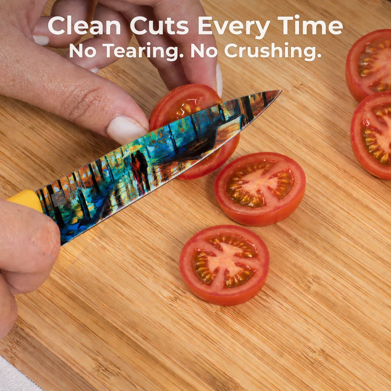 A person slices cherry tomatoes on a wooden cutting board with a vibrant knife from the Chef's Vision Masterpiece Six-Piece Knife Set; text reads, "Clean Cuts Every Time. No Tearing. No Crushing.