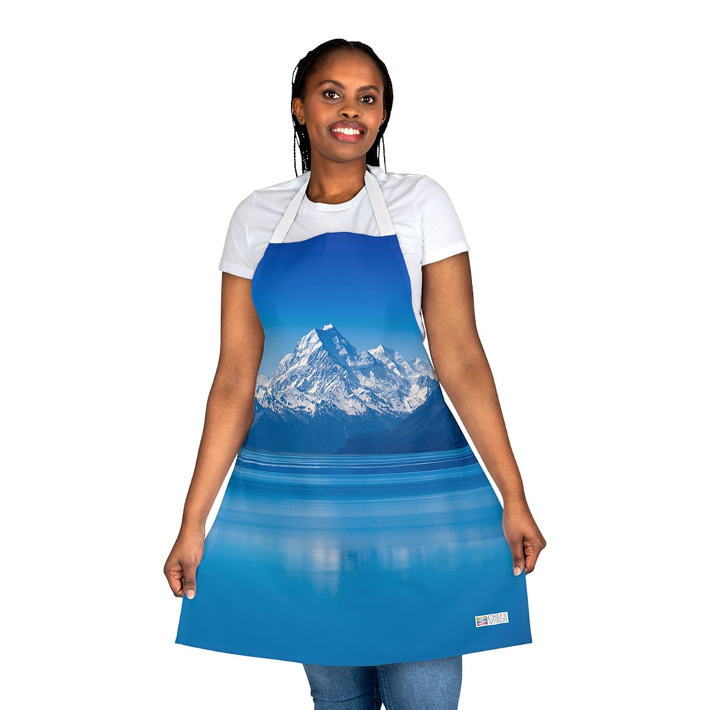 A woman wearing a Chef's Vision Landscape Apron with mountains in the background, showcasing the beauty of nature.