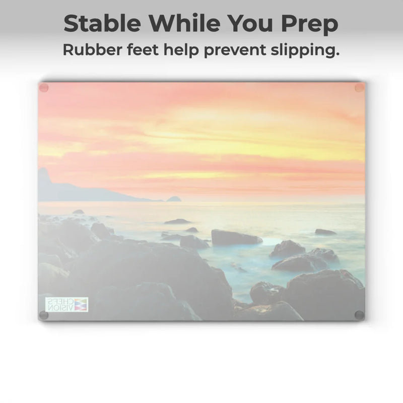 The Chef's Vision SliceBright Landscape Glass Cutting Board features a scenic seascape design and rubber feet on each corner for stability. Text reads: "Stable While You Prep. Rubber feet help prevent slipping.