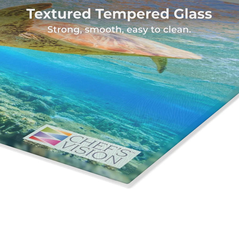 A corner of the SliceBright Wildlife Glass Cutting Board by Chef’s Vision features vivid underwater art, the Chef's Vision logo, and text: "Textured Tempered Glass. Strong, smooth, easy to clean." Functional kitchen art.