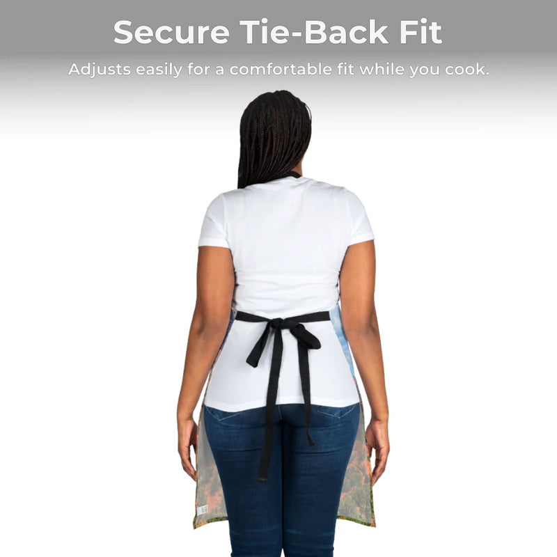 Person shown from the back wearing a white t-shirt, blue jeans, and the Chef's Vision Jurassic Apron. Text above: "Secure Tie-Back Fit: Adjusts easily for comfort while you cook—a unique gift for dino lovers.